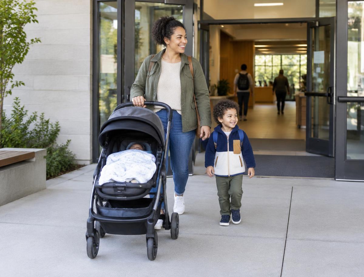 A parent arriving at a building entrance with a stroller and a young child.
